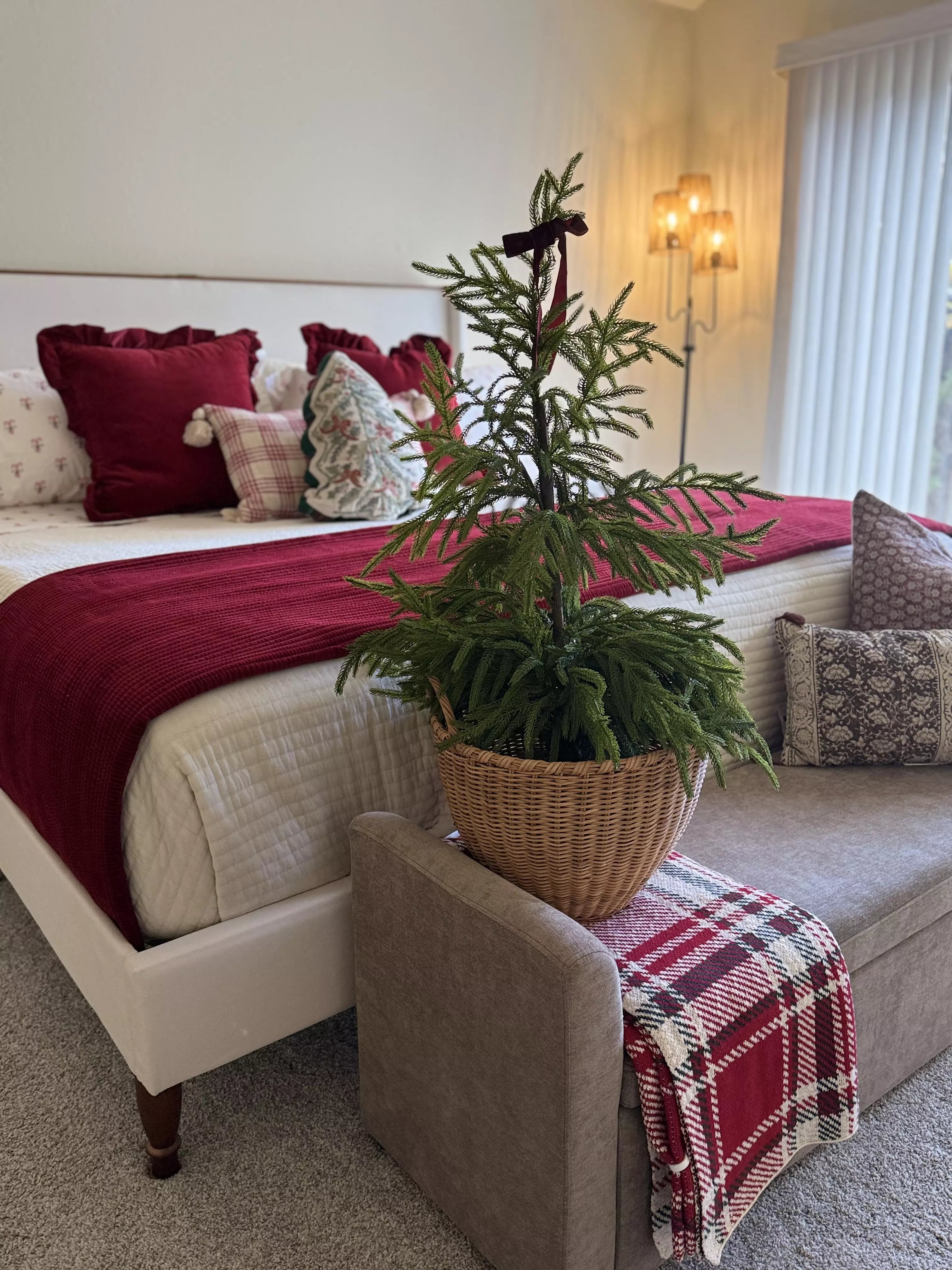 Decorative Christmas tree in a woven basket on a bed with red and plaid accents.