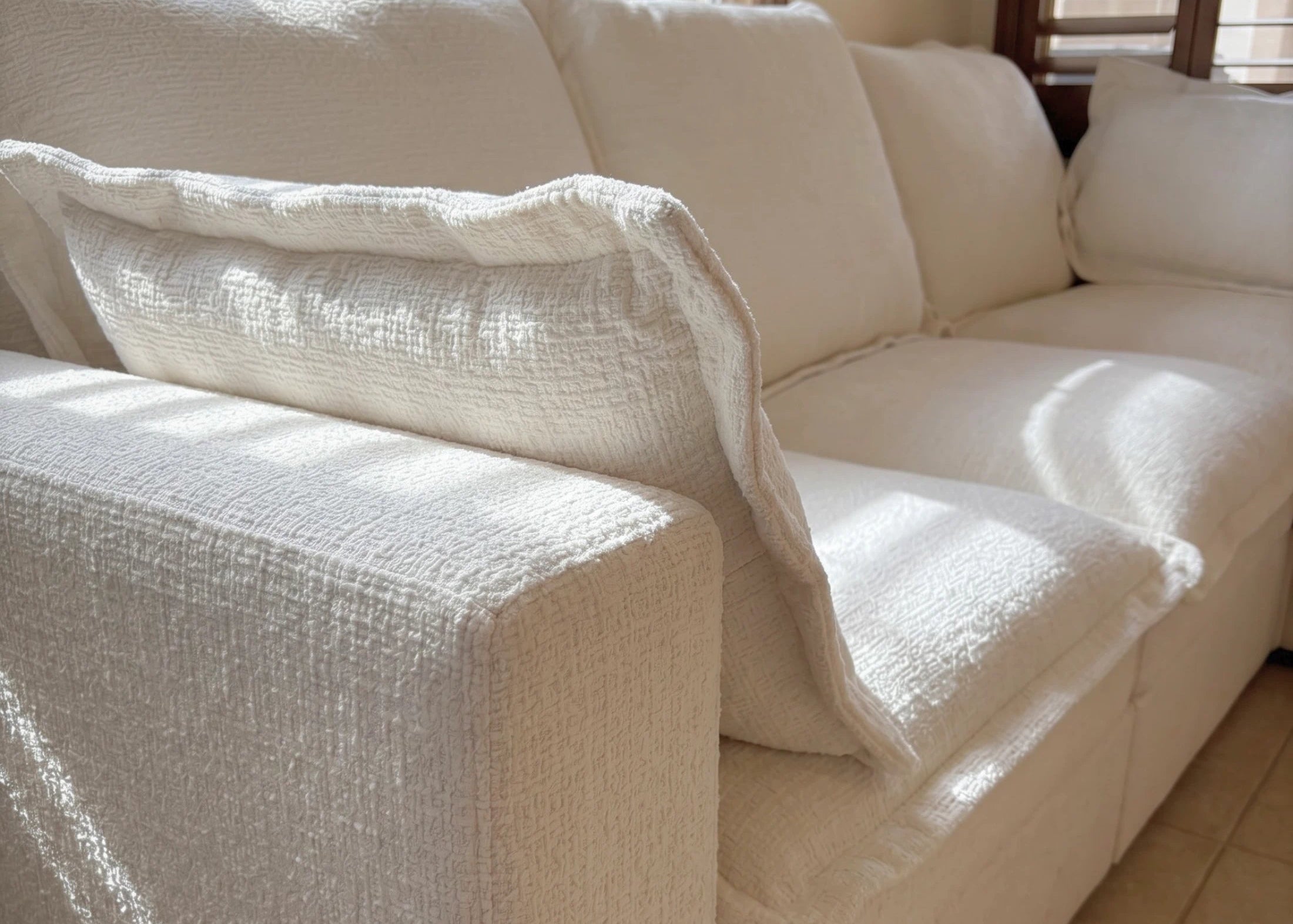 Beige sectional sofa with a textured cover in a room with windows and blinds.