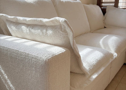 Beige sectional sofa with a textured cover in a room with windows and blinds.