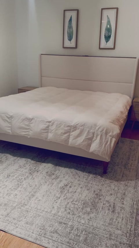 Load video: Beige bed with white bedding in a room with framed artwork on the wall.